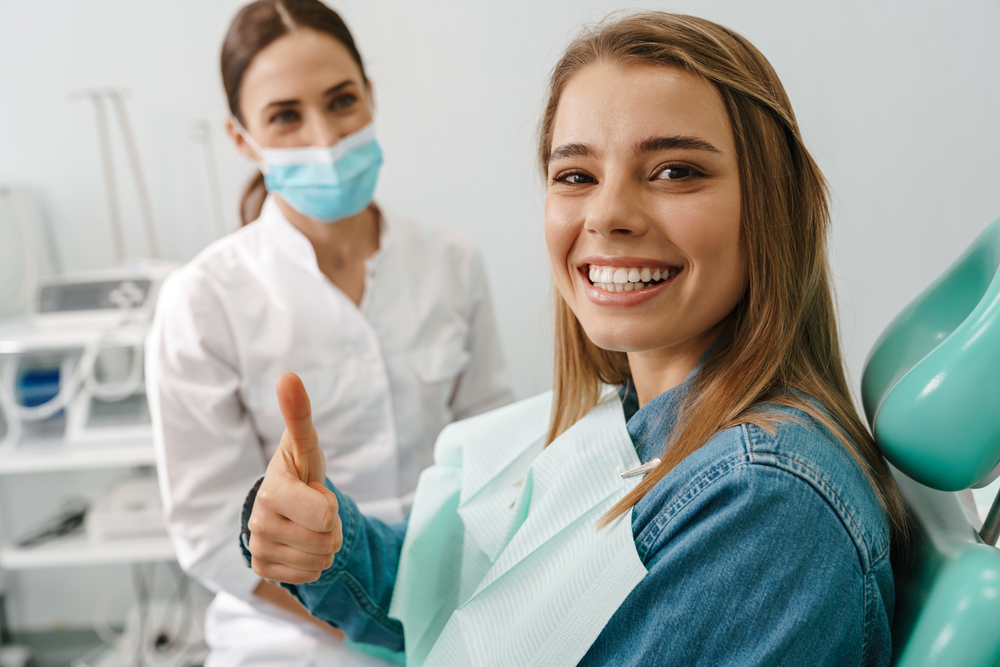 a lady is smiling and showing thumbs up after getting dental treatment
